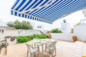 A patio with a striped awning, white chairs, and a table set for dining. - Apartamento Sol by C diz Time (Conil de la Frontera)