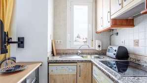 A compact kitchen with a dishwasher, stove, toaster, and a window with a view of a building. - Apartamento Sue o by C diz Time (Conil de la Frontera)