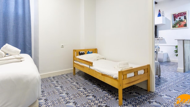 Een kamer met een houten bed, een vloer met blauw patroon en een witte muur.