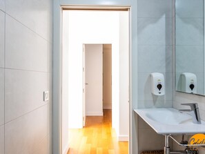 Une salle de bain moderne avec un lavabo blanc, un miroir et des distributeurs de gel hydroalcoolique.