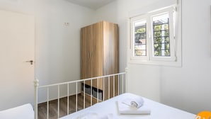 Quarto com cama, guarda-roupa de madeira, janela com persianas e porta branca.