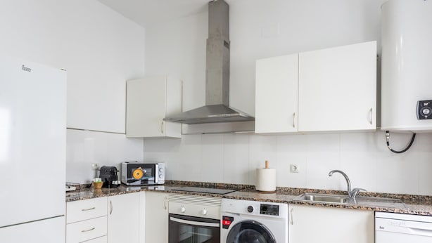 Une cuisine moderne avec des meubles blancs, un four encastré, un lave-linge, un four à micro-ondes et une machine à café.