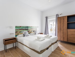 Ein modernes Schlafzimmer mit zwei Betten, einem Holzschrank und einem farbenfrohen, abstrakten Gemälde an der Wand.