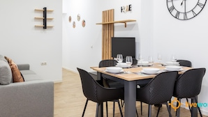 Un espace repas moderne avec une table en bois dressée pour quatre personnes, des chaises noires et une grande horloge murale.