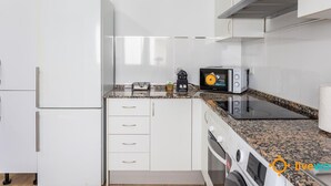 Une cuisine compacte avec des meubles blancs, un four à micro-ondes, un grille-pain et un lave-linge.