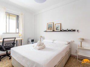 A hotel room with a bed, a desk, a chair, a heater, a shelf with pictures, and a lamp. - Teresa Uno by Cadiz Time (Cádiz)
