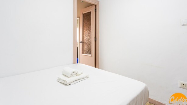 A hotel room with a bed, a door with a textured panel, and a small blue object on the floor. - Teresa Uno by Cadiz Time (Cádiz)