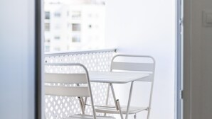 Varanda de metal branca com uma mesa e uma cadeira, com vista para um edifício.