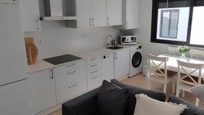 A modern kitchen with white cabinets, a microwave, and a washing machine. There is a dining area with a table and chairs. - Cruces by Livework in El Puerto de Santa Mar a (El Puerto de Santa Maria)