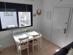 Ett rum med ett matbord och stolar, ett fönster med persienner, en dörr och en väggmonterad ljusströmbrytare.