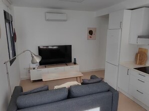 Ett modernt vardagsrum med en grå soffa, en platt-TV, ett vitt skåp och ett litet bord.