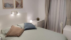 A bedroom with a bed, bedside tables, a nightstand, a lamp, and a chair. There are two framed pictures on the wall. - Cruces by Livework in El Puerto de Santa Mar a (El Puerto de Santa Maria)