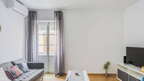 Una sala de estar moderna con un sofá gris, una mesa de centro, un televisor sobre un mueble blanco y una planta en maceta.