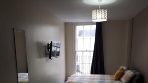 A hotel room with a bed, a desk, a chair, a TV, and a window with a view. - Chic Studio in Cheltenham (Cheltenham)