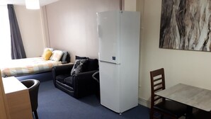 A compact hotel room with a bed, a sofa, a dining table, a chair, and a refrigerator. - Chic Studio in Cheltenham (Cheltenham)