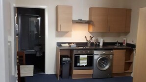 A compact kitchen with a washing machine, oven, and a small countertop. - Chic Studio in Cheltenham (Cheltenham)