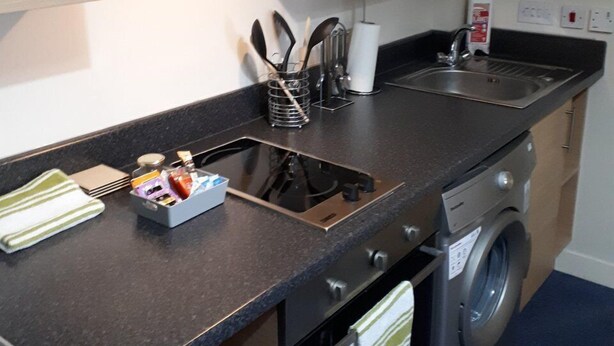 A compact kitchen with a sink, stove, oven, and a washing machine. - Chic Studio in Cheltenham (Cheltenham)