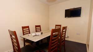 Ein Esszimmer mit Tisch, Stühlen, einem an der Wand montierten Fernseher und einer Steckdose.