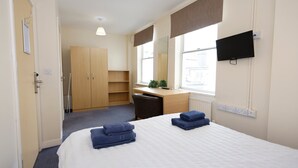 Ein Hotelzimmer mit Bett, Schreibtisch, Stuhl, Kleiderschrank, Fernseher und Fenster.