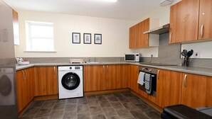 A compact kitchen with wooden cabinets, a washing machine, a microwave, and a stove. - Restful Retreat in Cheltenham (Cheltenham)