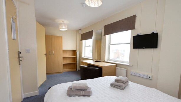 Ein Hotelzimmer mit Bett, Schreibtisch, Kleiderschrank, Spiegel und Fernseher.