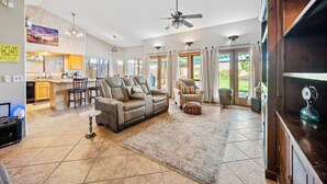 A spacious living room with a large sofa, a coffee table, and a fireplace. There is a kitchen area with a dining table and chairs visible in the background. - SANCTUARY IN THE SUN, 
great location to go or stay (Mesa)