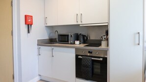 A compact kitchen with white cabinets, a microwave, a kettle, and a toaster.