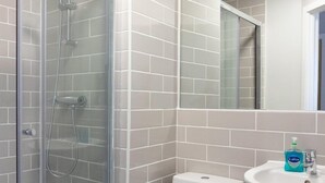 A bathroom with a glass shower enclosure, a white toilet, and a sink with a mirror above it.
