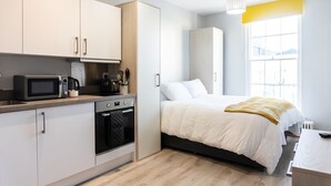 A compact bedroom with a bed, a small kitchenette, and a window with a view.