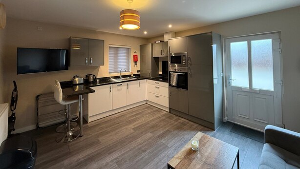 A modern kitchen with a flat-screen TV, stainless steel appliances, and a bar stool. - Cosy 2-bedroom Flat close to Royal Holloway (London)