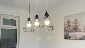 Un coin repas avec une table ronde dressée pour quatre personnes, des chaises noires et un tableau représentant des arbres accroché au mur.