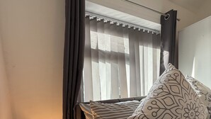Une chambre à coucher bien rangée, avec un lit, des oreillers, une lampe de chevet et une fenêtre avec des rideaux.