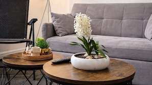 Un salon moderne avec un canapé gris, un lampadaire, un tableau et une orchidée en pot posée sur une table basse.