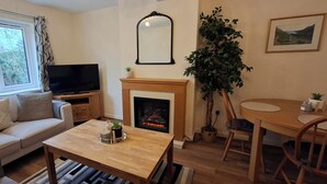 En stue med sofa, tv, pejs, spisebord, stole og en stor plante.