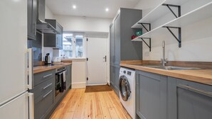 A modern kitchen with grey cabinets, a wooden countertop, a built-in washing machine, and a window providing natural light. - Jeeves Hideaway - sleeps 2 guests  in 1 bedroom (Old Hunstanton)