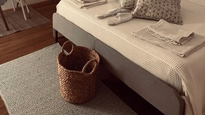 A neatly made bed with pillows and folded towels, a bedside table with a lamp, a woven basket, and a door with a light switch. - The Master's Suite [In the heart of the Borgo] (Bienno)