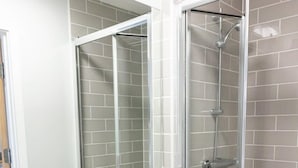 Un baño con lavamanos blanco, un espejo, ducha con puerta de cristal y un cubo de basura.