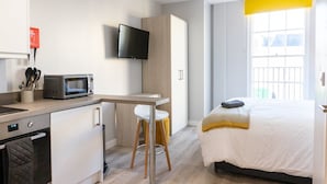 Una habitación de hotel moderna con kitchenette, una cama, un televisor y un ventanal grande.