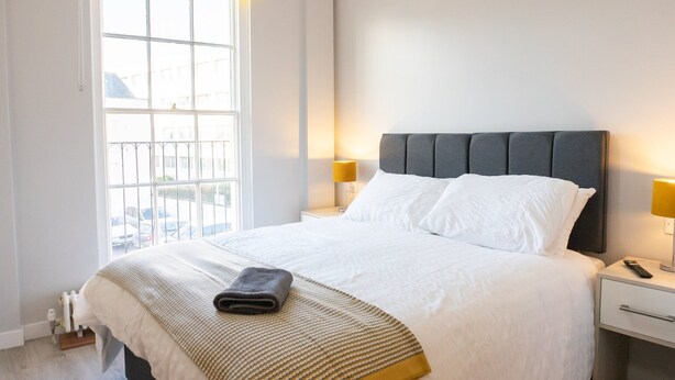 Habitación de hotel con cama, mesita de noche, lámpara y ventana con vistas.