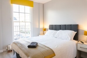 A hotel room with a bed, a nightstand, a lamp, and a window with a view. - Chic Studio in Cheltenham (Cheltenham)