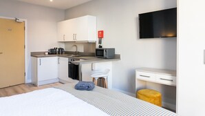 Una habitación de hotel compacta con kitchenette, una cama, un televisor y un taburete pequeño.