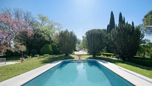 A rectangular swimming pool with a clear blue water surface, surrounded by well-maintained grass and various trees, including tall conifers and flowering shrubs. - Bed and Breakfast 'Chambre 'Cousin Paul'' with Shared Pool, Wi-Fi and Air Conditioning (Verfeil)