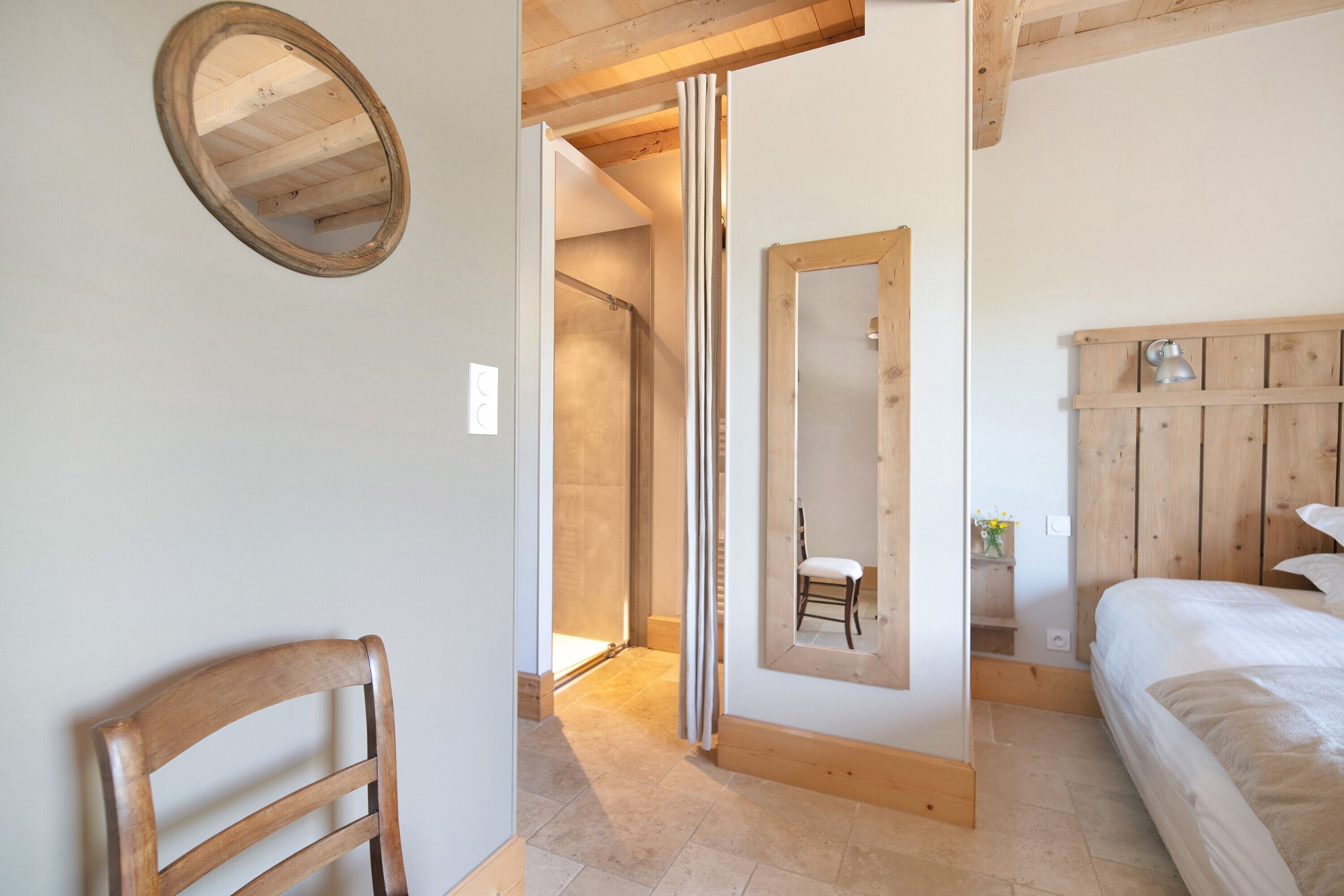 A bedroom with a wooden headboard, a bed, a chair, a mirror, and a wooden door.