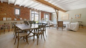 A spacious dining area with a rustic brick wall, wooden ceiling beams, and a large table surrounded by chairs. - Bed and Breakfast 'Chambre 'Cousin Paul'' with Shared Pool, Wi-Fi and Air Conditioning (Verfeil)