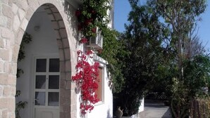 A building with a stone facade, a white door, and red flowers. - ARETHOUSA (Milos)