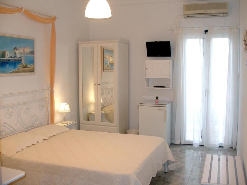 A bedroom with a bed, a wardrobe, a television, and a window with curtains.
