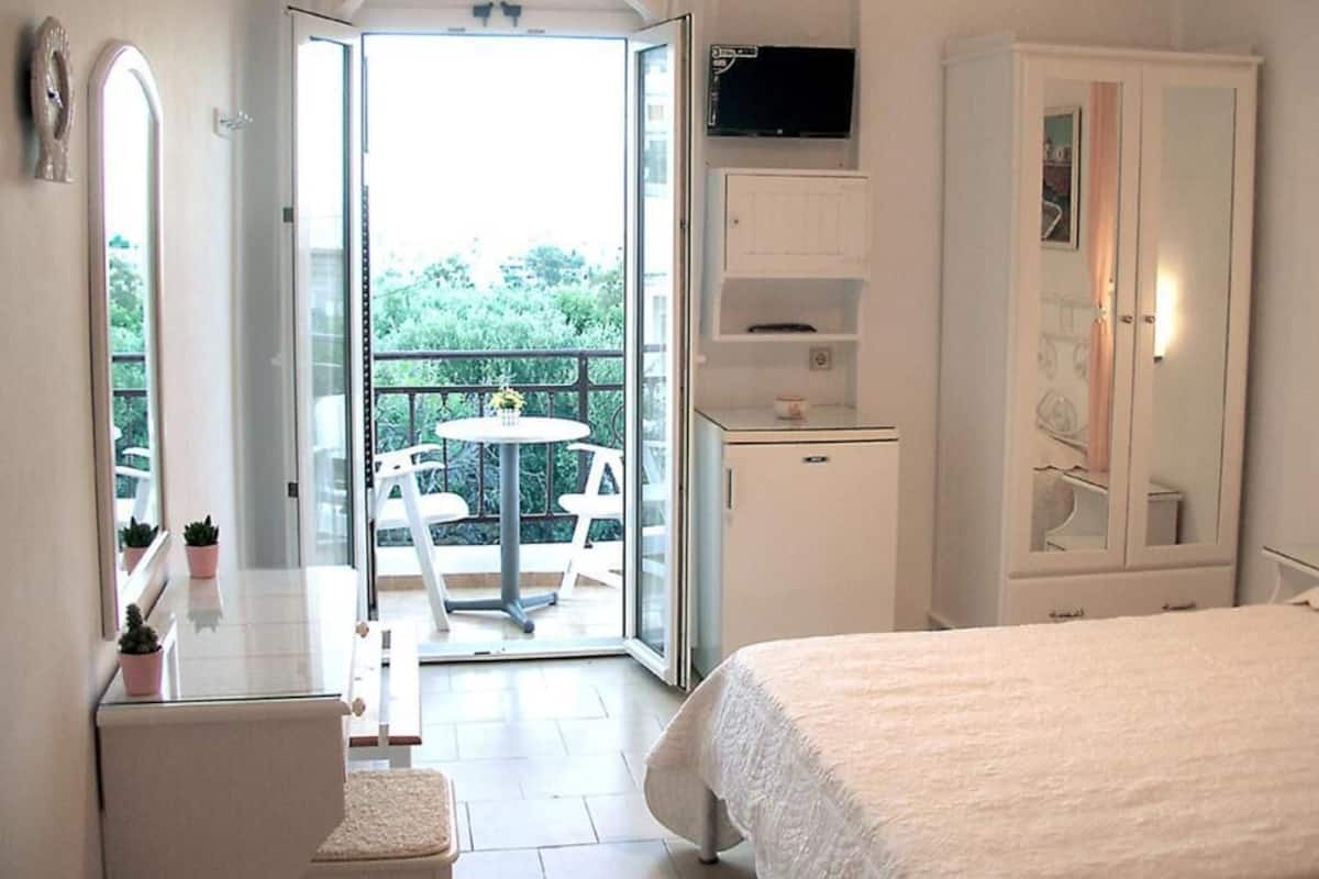 A bedroom with a bed, a wardrobe, a small table with chairs, and a balcony with a table and chairs.