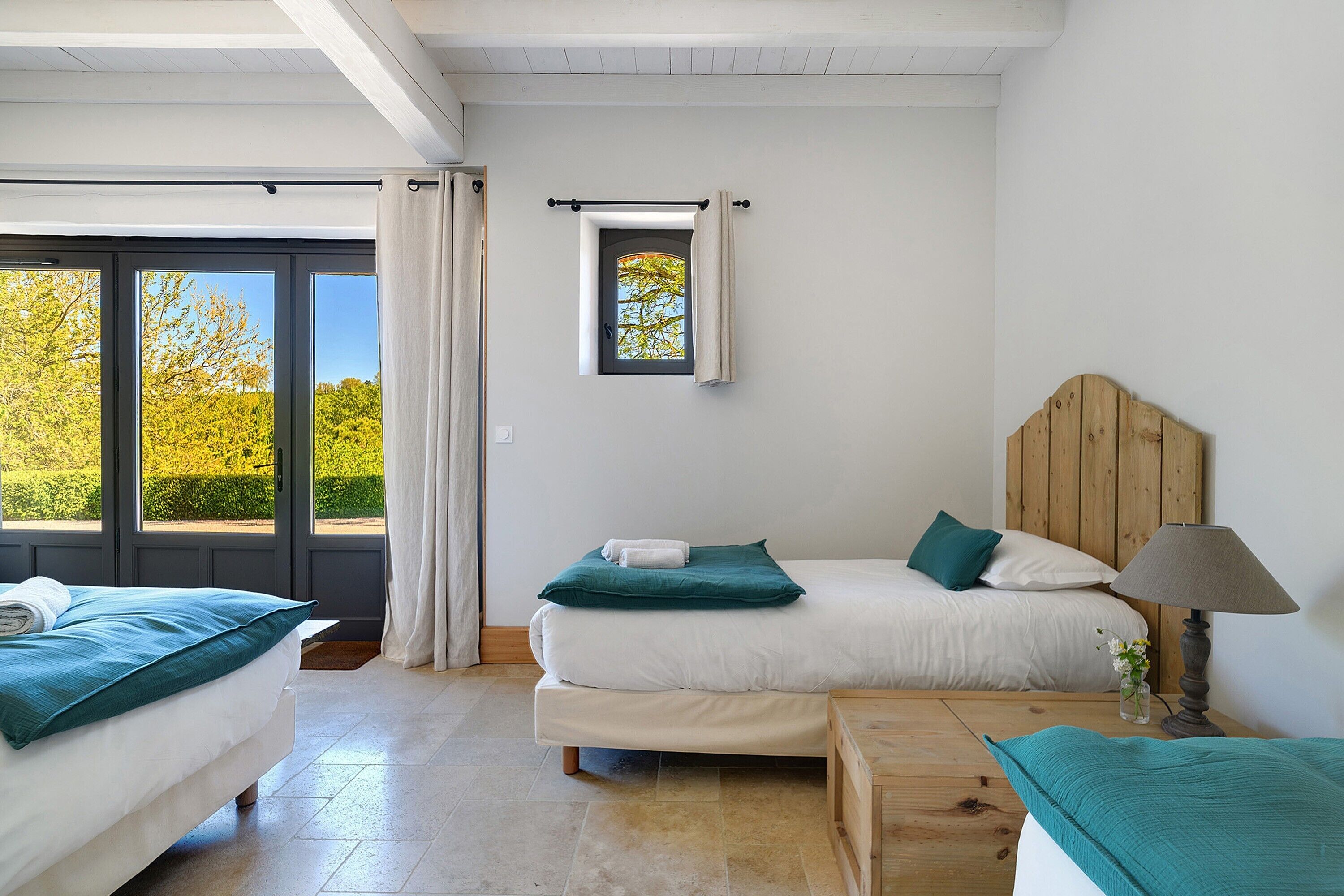 A bedroom with two beds, a window, and a small table with a lamp.