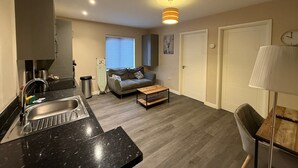 En kompakt opholdsstue med tekøkken, sofa, sofabord og lampe.