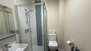 Casa de banho com chuveiro em cabine de vidro, lavatório branco, sanita e porta-toalhas.